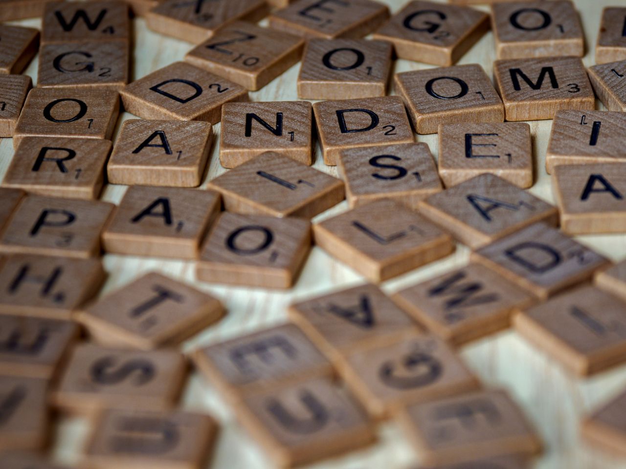 A close-up photo showing scattered wooden Scrabble tiles with letters and point values.