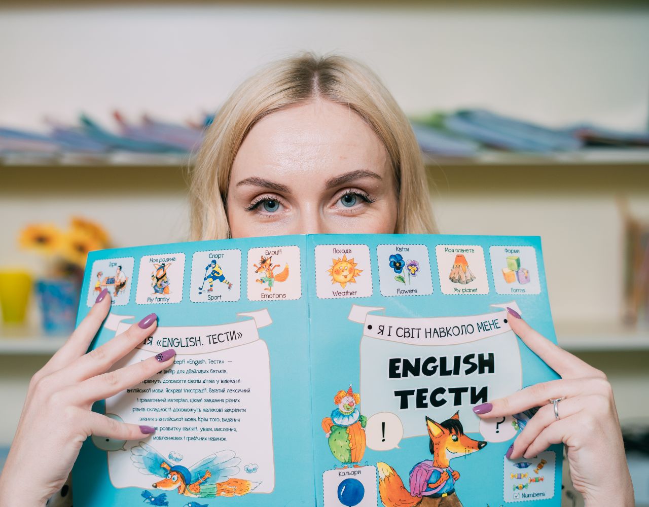 team-03 Blonde woman holding and reading an illustrated English book indoors.