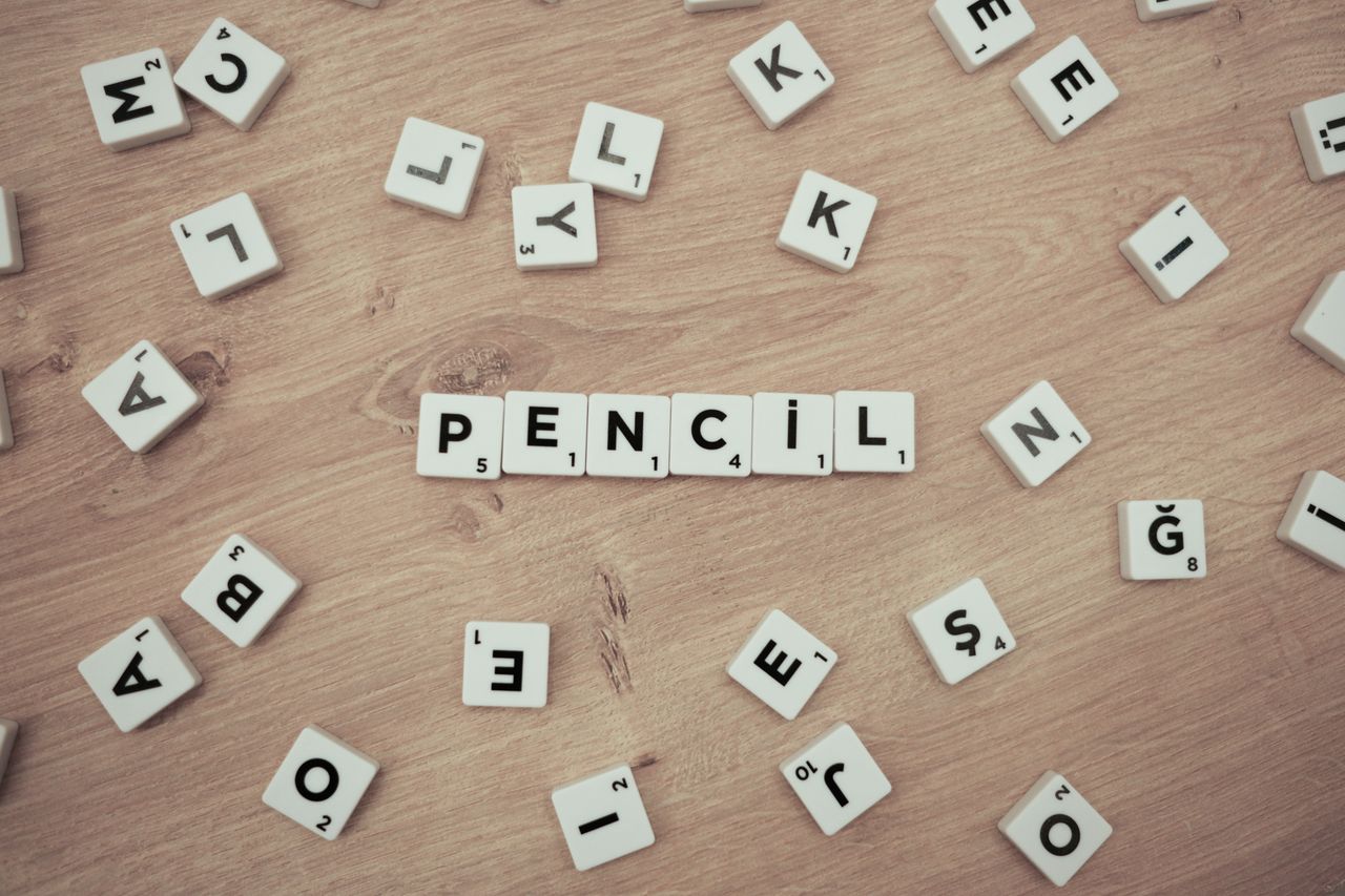 Wooden surface with scattered Scrabble tiles forming the word Pencil.