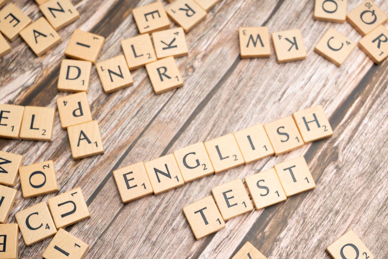 Wooden Scrabble tiles spelling out English Test on a wooden background, ideal for language exam themes.